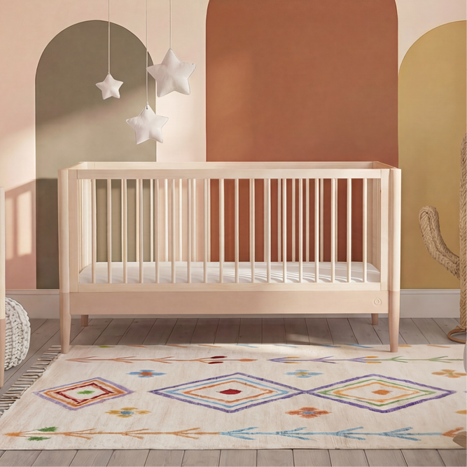 Gaia Baby Eos Cot Bed in natural wood with powder blush accents, featuring a sturdy design and slatted sides for safety.