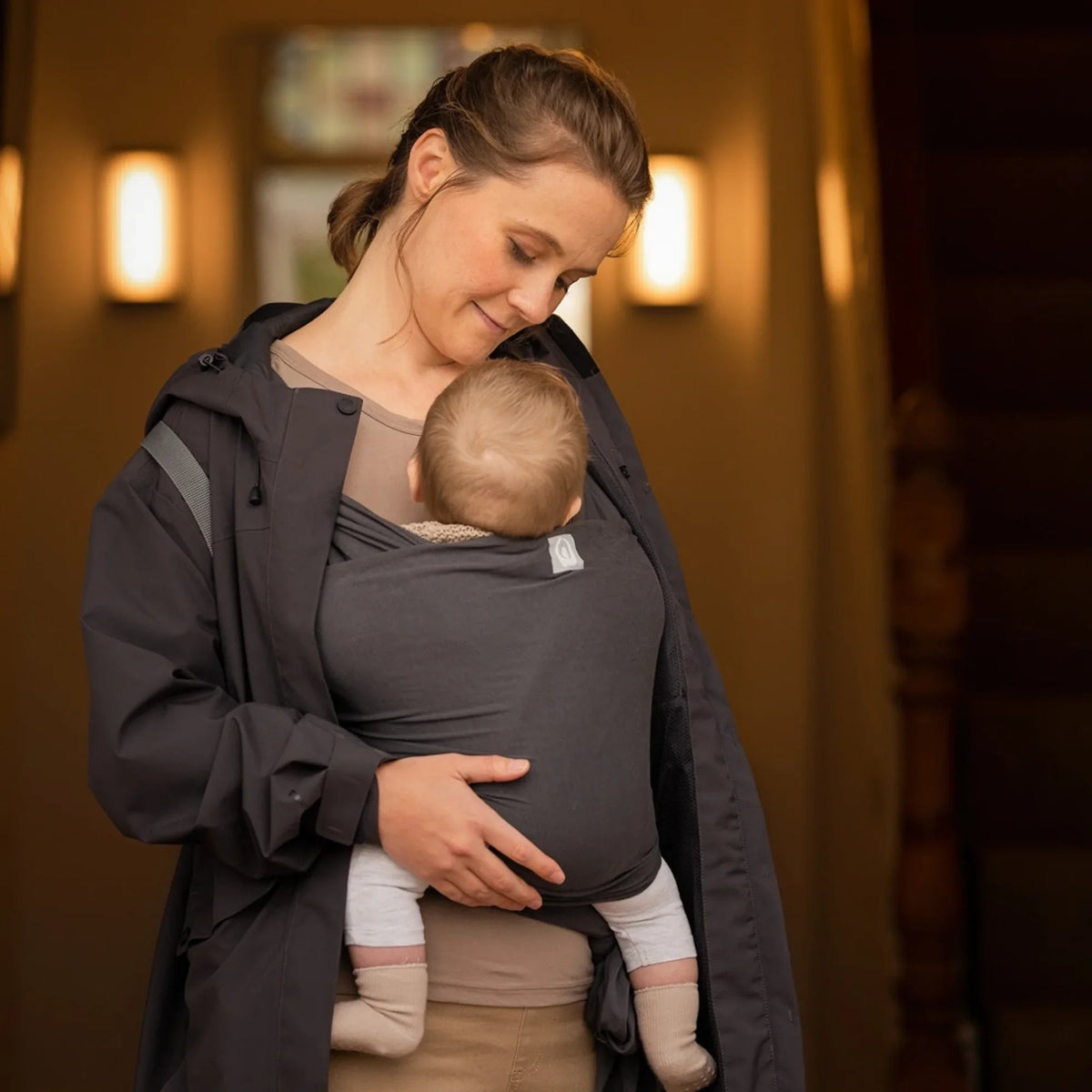 Gaia Baby stretchy baby wrap in graphite, shown worn around a parent for comfortable, secure baby carrying.