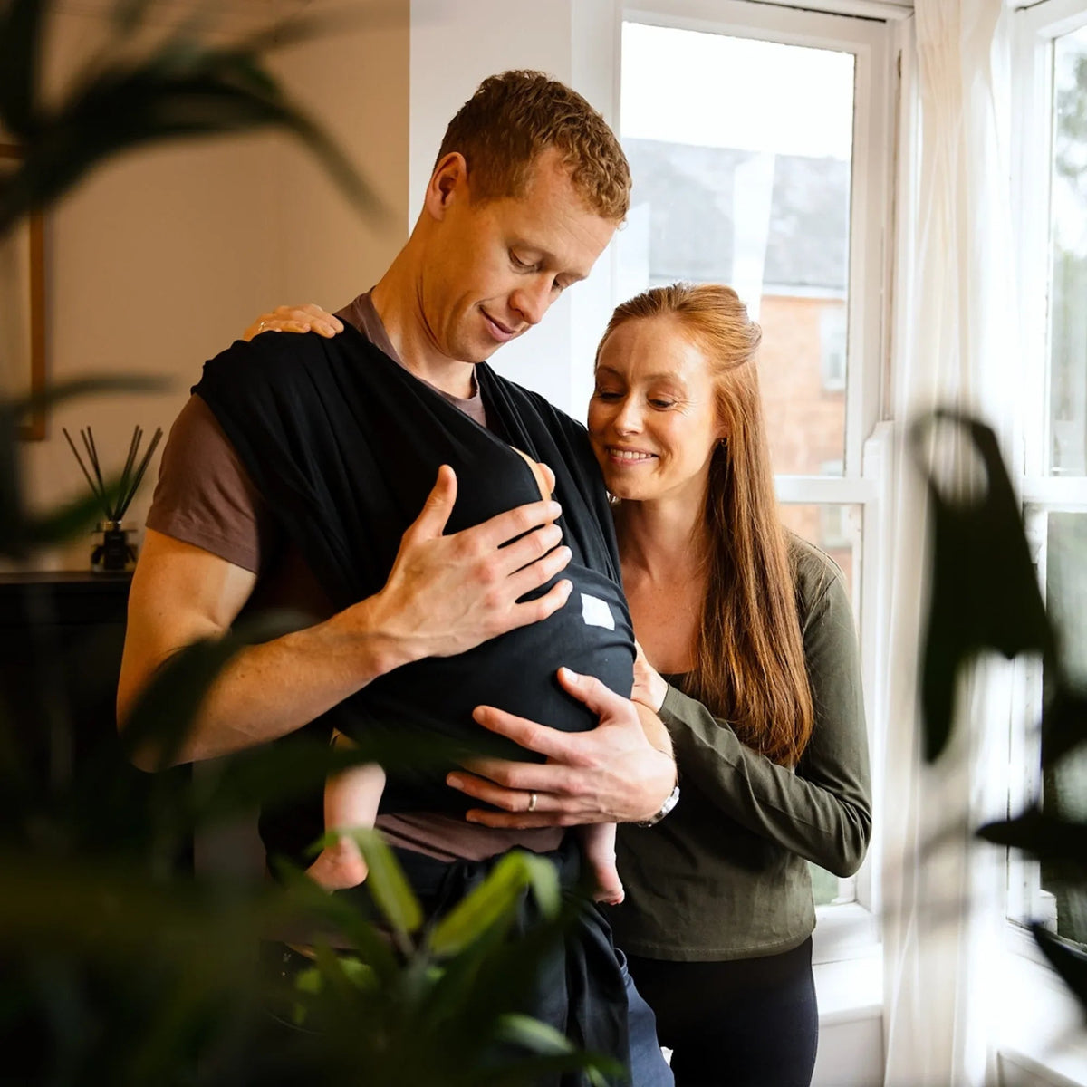 Gaia Baby stretchy baby wrap in ebony worn by a couple, showcasing comfortable and flexible babywearing accessories.