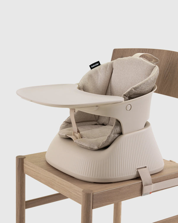 Hannie portable high chair in White Sand color, featuring a sleek design with adjustable safety straps and sturdy legs.