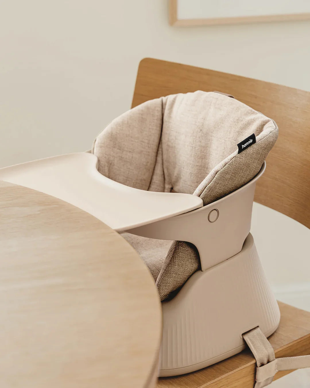 Hannie portable high chair in White Sand color, compact design with safety straps, suitable for feeding infants and toddlers.